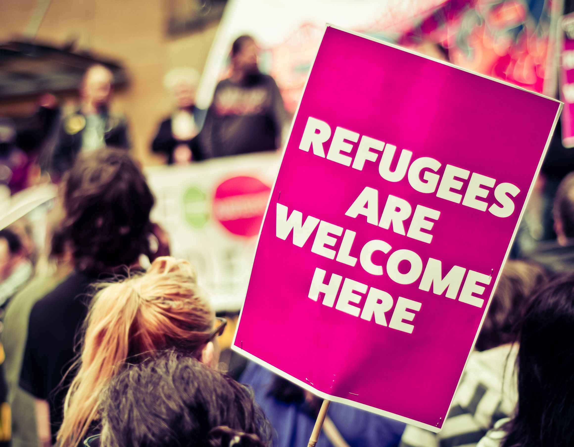 A crowd of people with a sign reading "Refugees Are Welcome here"