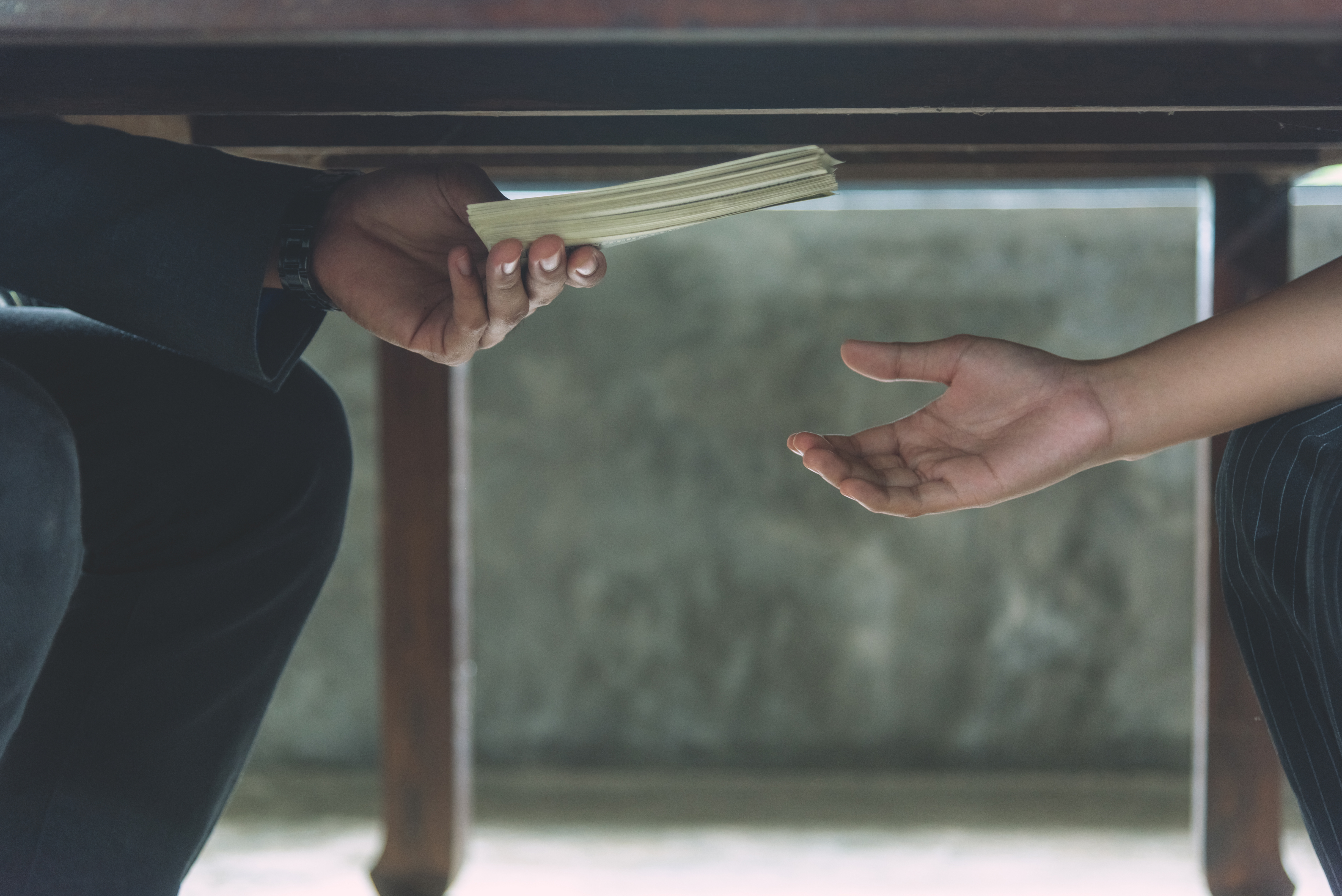 hands passing cash under a table