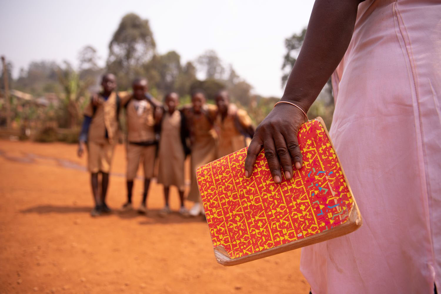 An african teacher is holding a book with her students out of focus in the background, concept of education in africa