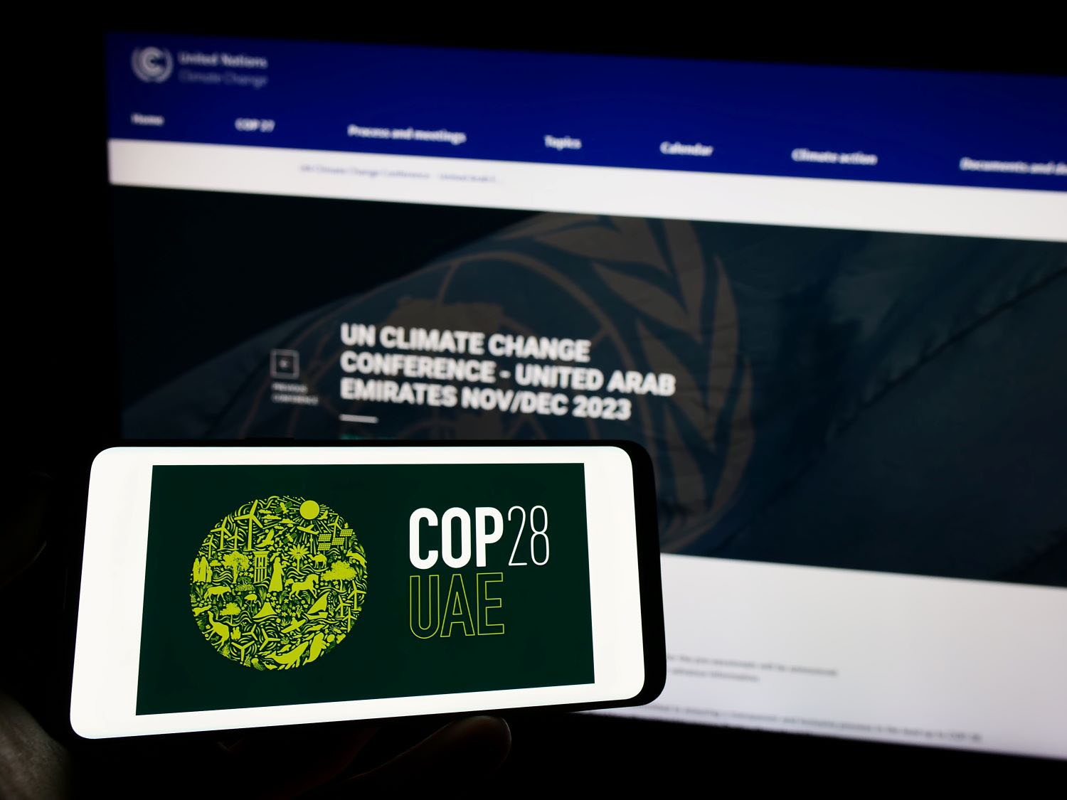 Person holding cellphone with logo of UN climate change conference COP28 (Dubai) on screen in front of webpage.