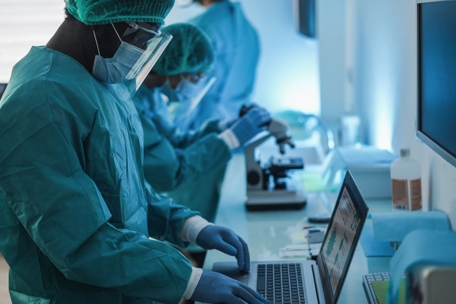 Medical workers in hazmat suit working with computer and micoroscope inside laboratory hospital