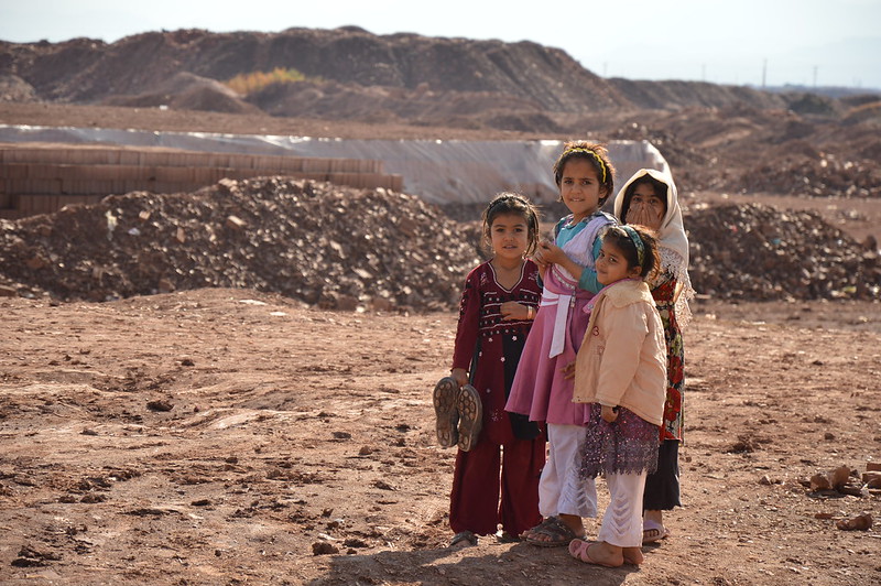 Refugee girls in rocky terrain look at camera and smile 