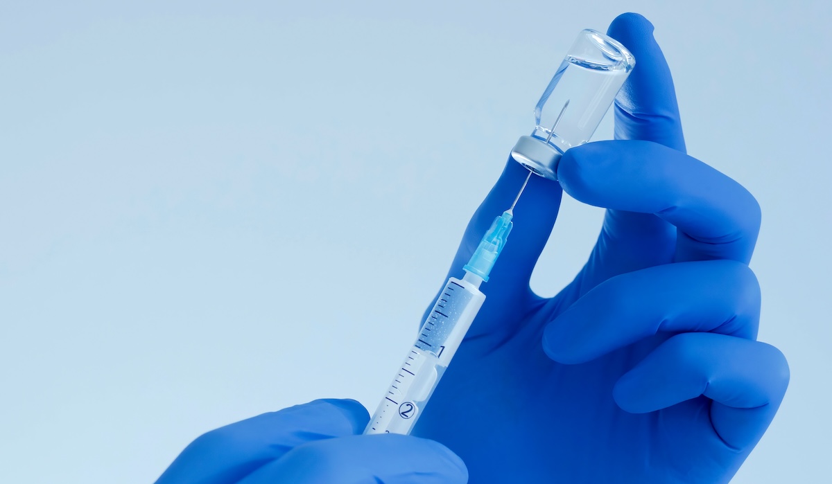Gloved hands preparing a syringe with a vaccine