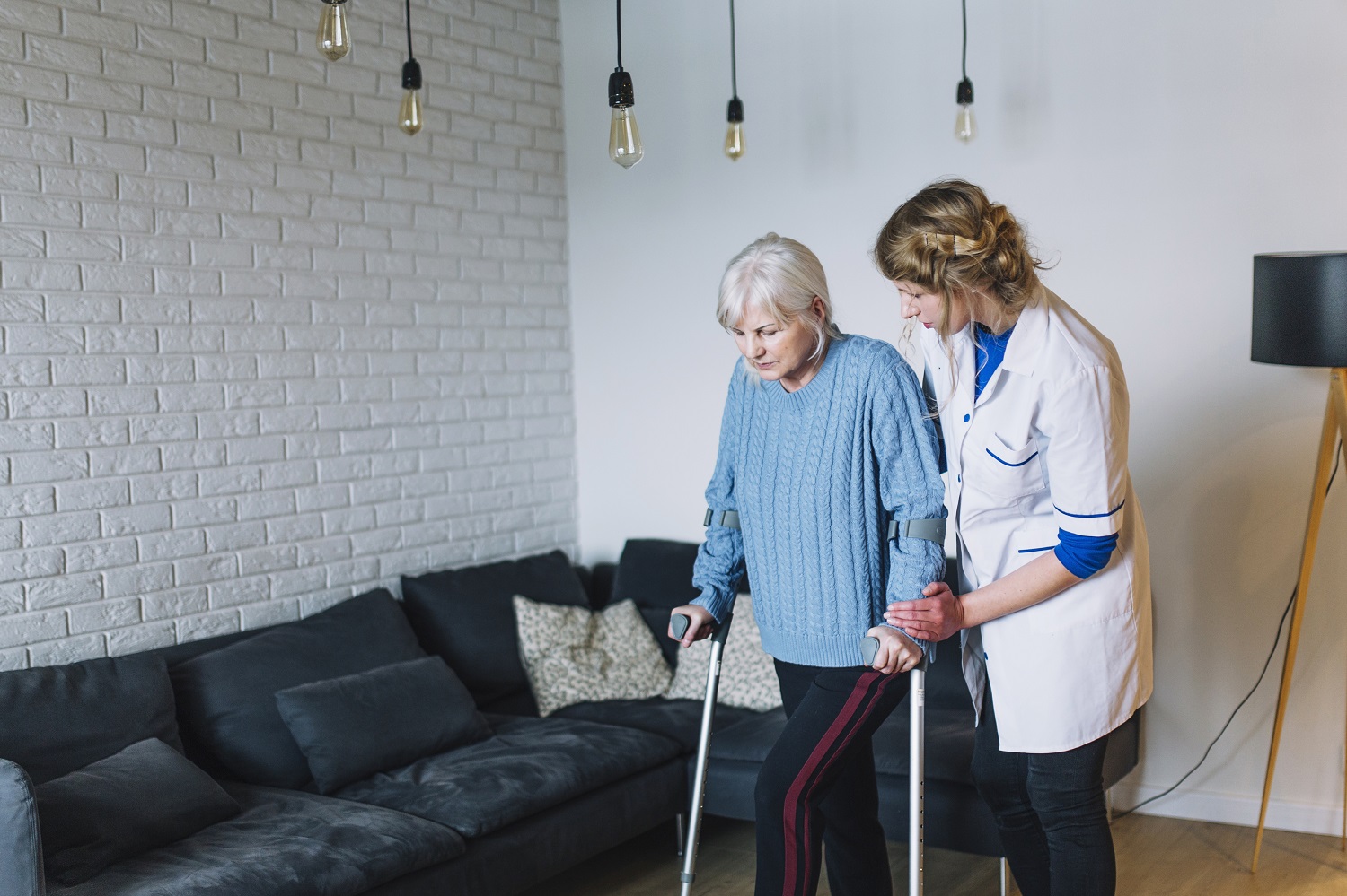 Caregiver helps elder woman walk on crutches