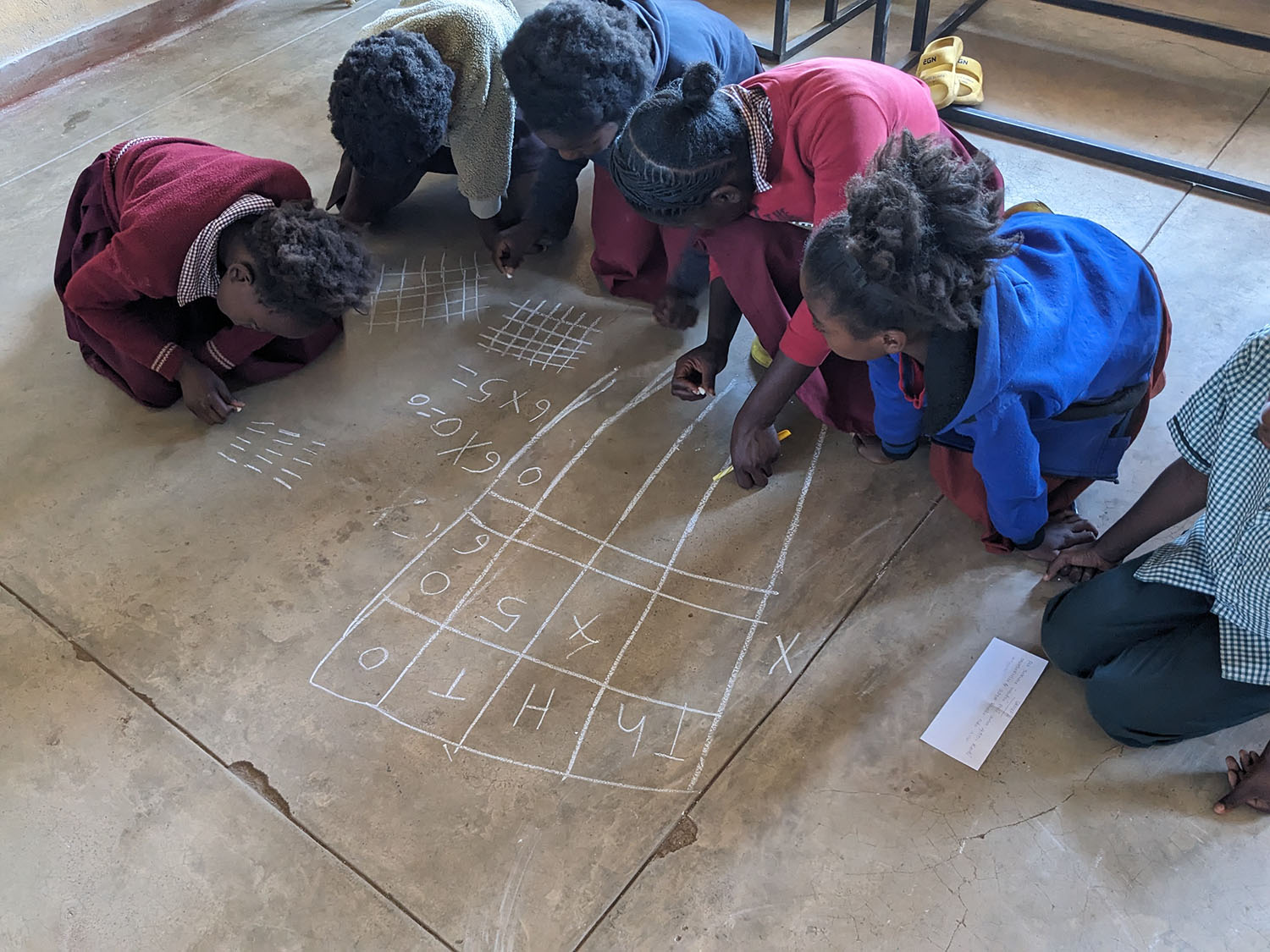 Children using chalk on the floor to solve 3 digit multiplication problems