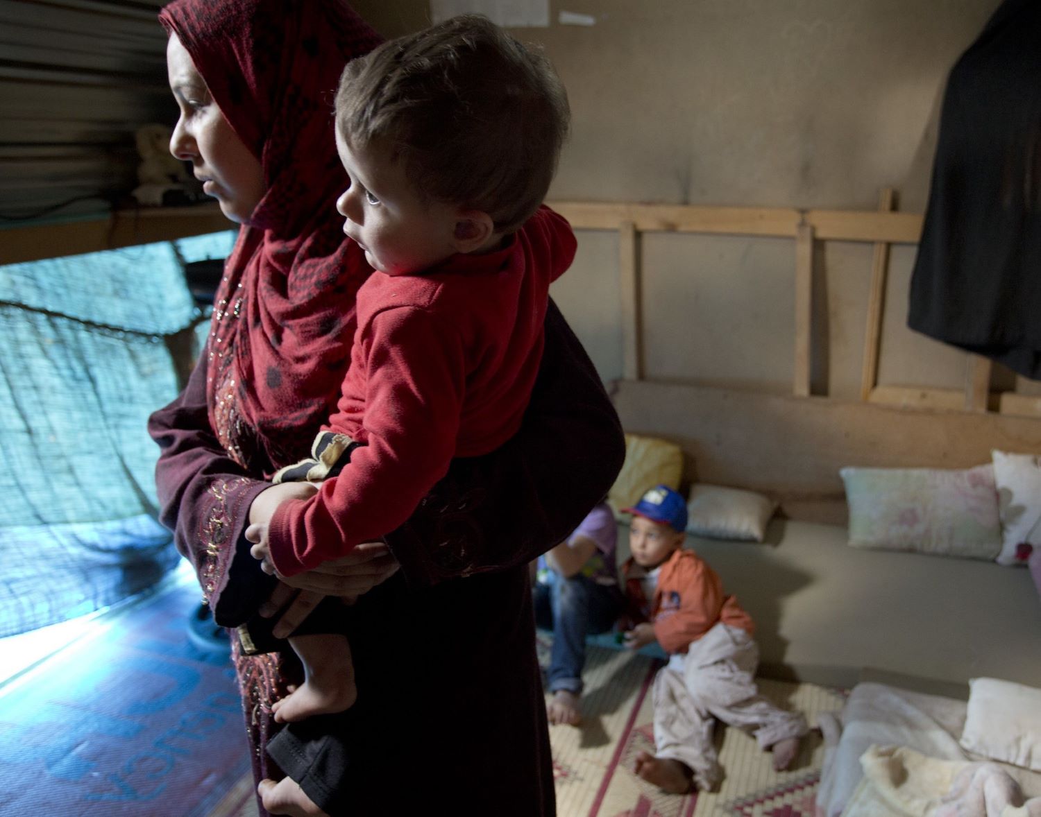 Syrian refugee, Elham Salim (far left) holds her son Ahmad in their makeshift home