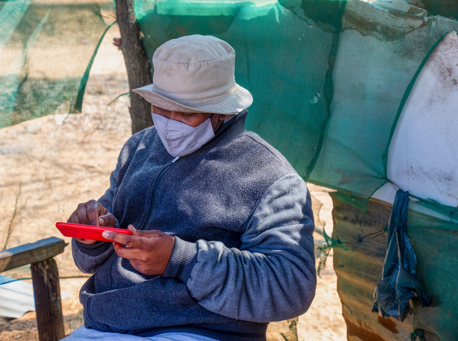 Older man wearing a mask using the phone in a shed