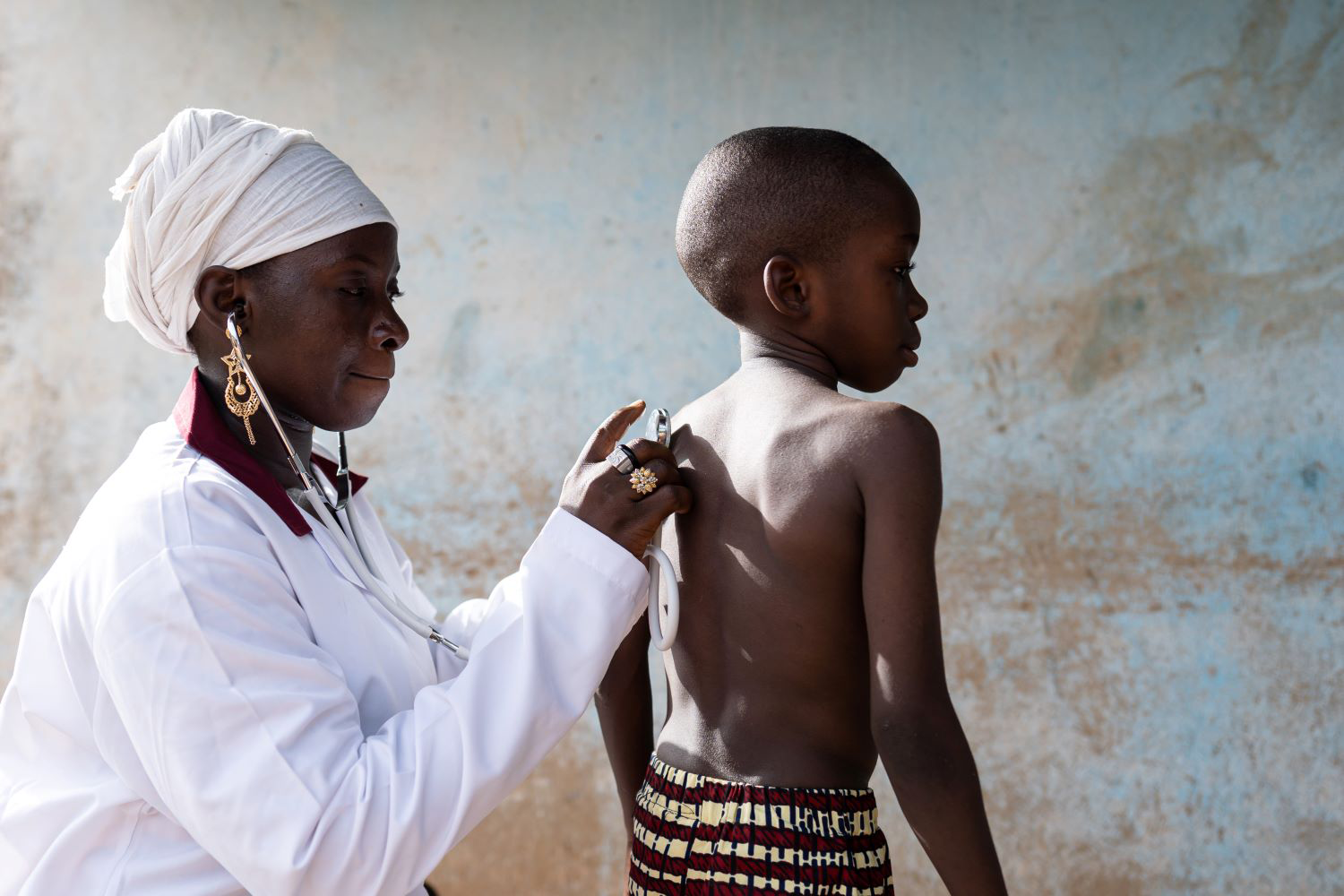 Doctor placing a stethoscope on the bare back of a standing schoolboy during a routine screening
