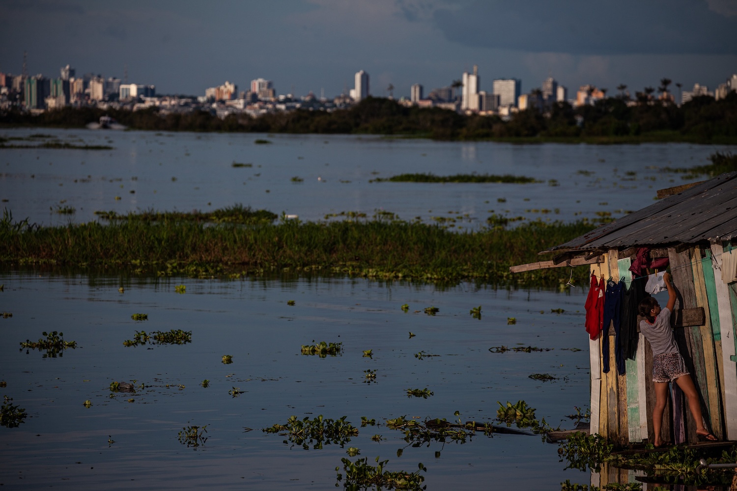 A young woman arranges clothes on the clothesline of her house, a floating one located on the banks of the Rio Negro