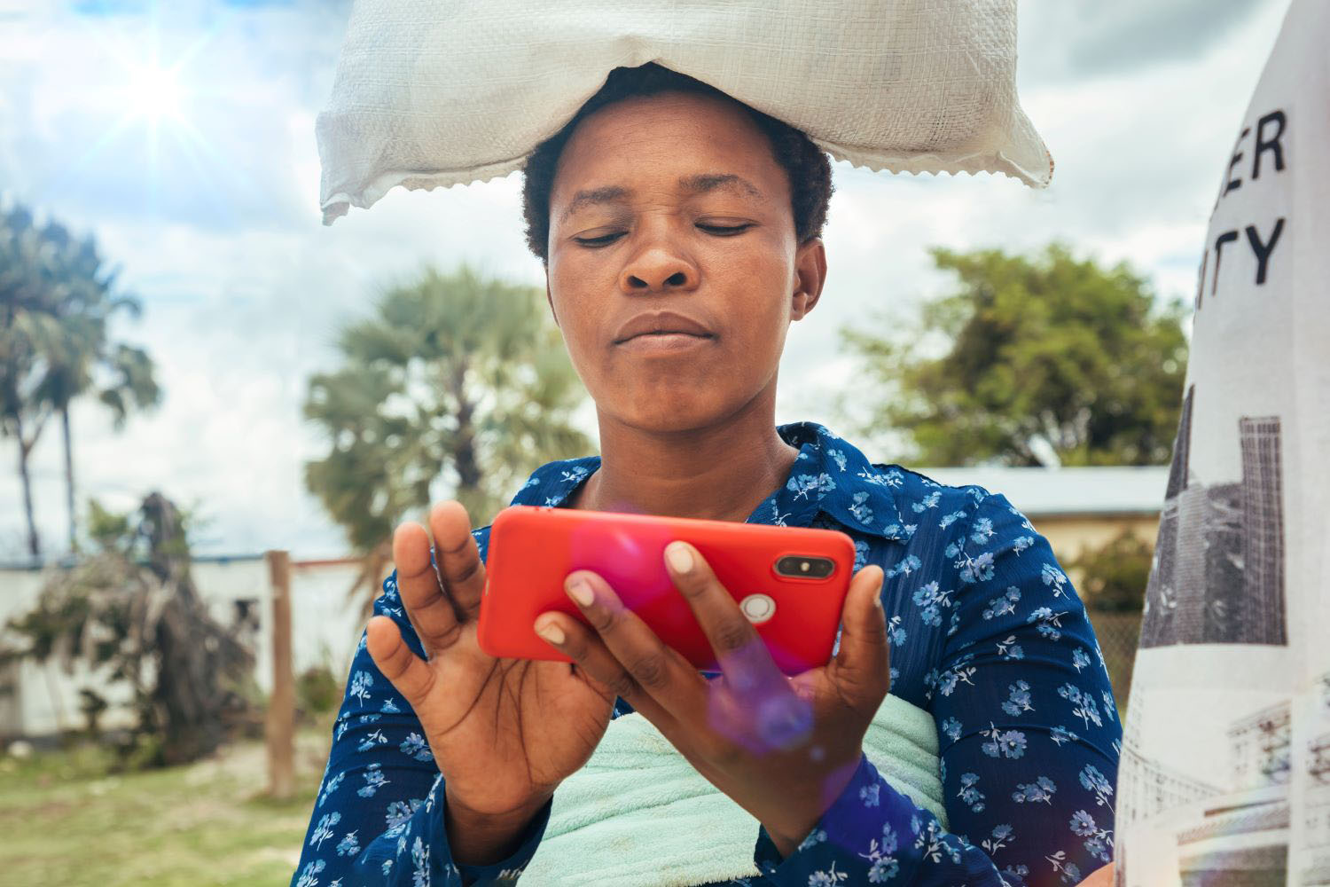African woman using her phone while carrying her child on her back