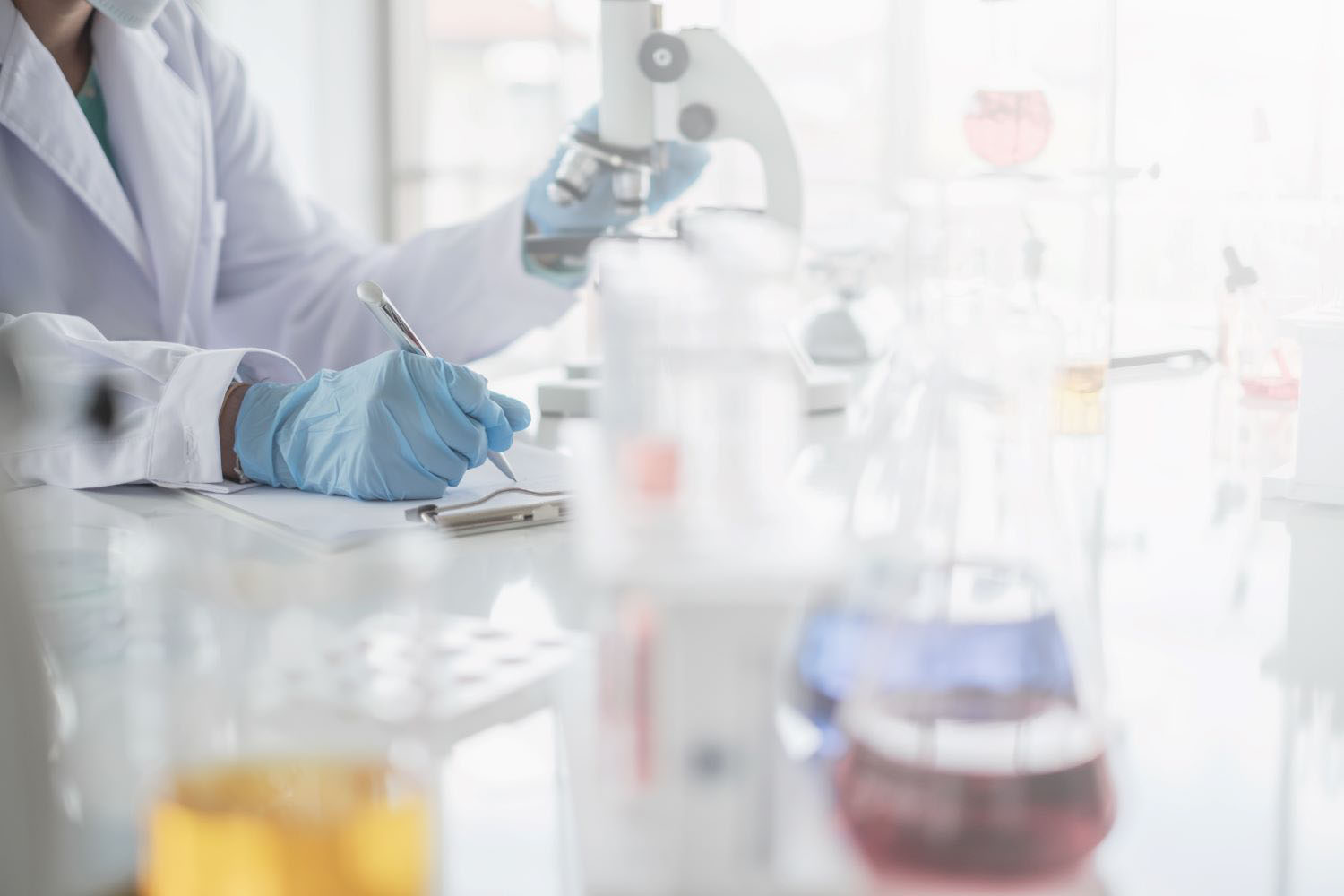 A scientist hands writing on a clipboard in laboratory with test tube microscope and solutions