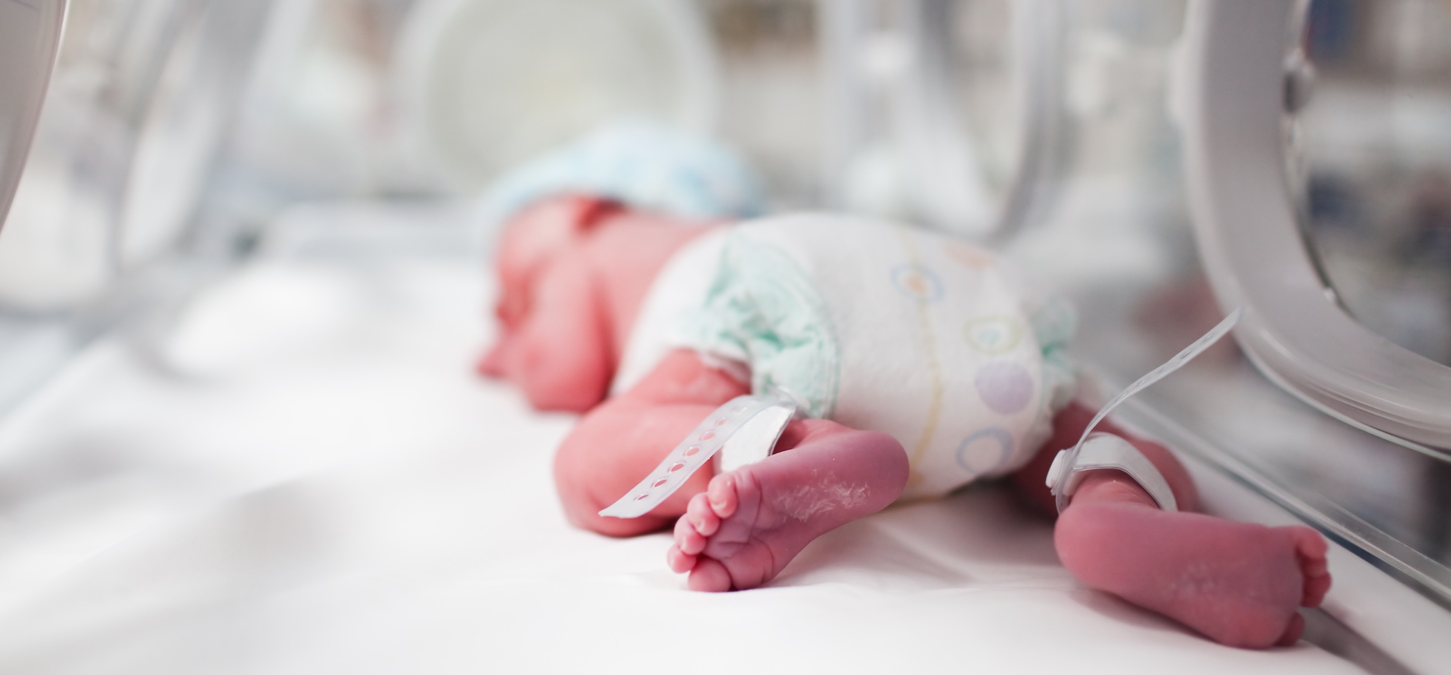 Newborn baby boy covered in vertix inside incubator