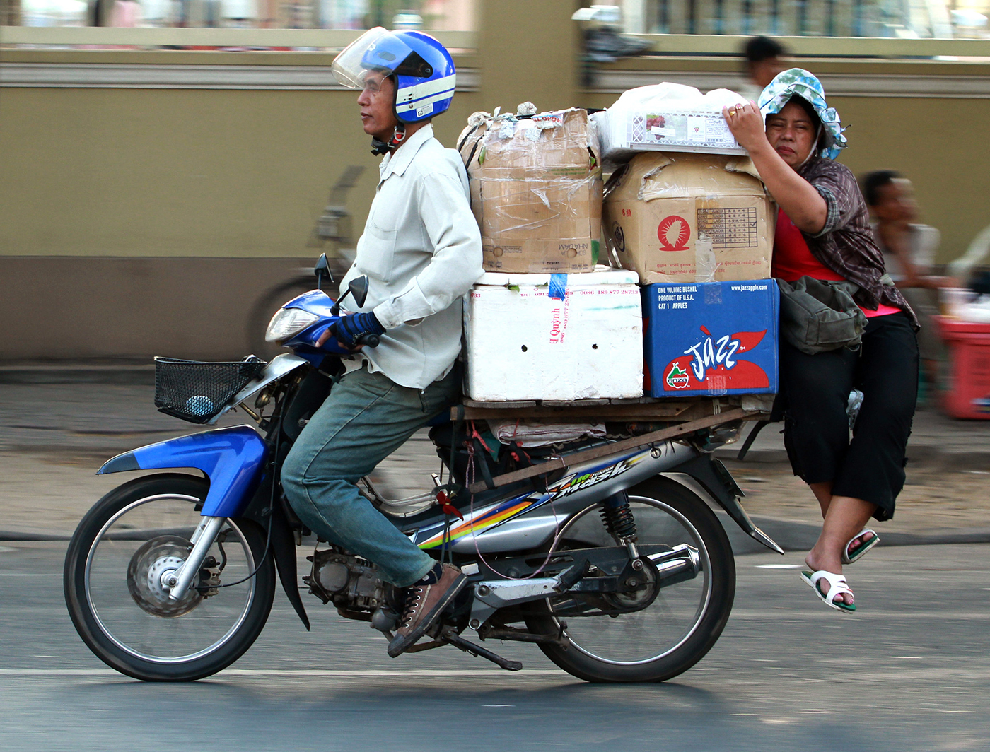 A motorcycle 'taxi' driver transports a trader and dry goods to the Phnom Penh market.