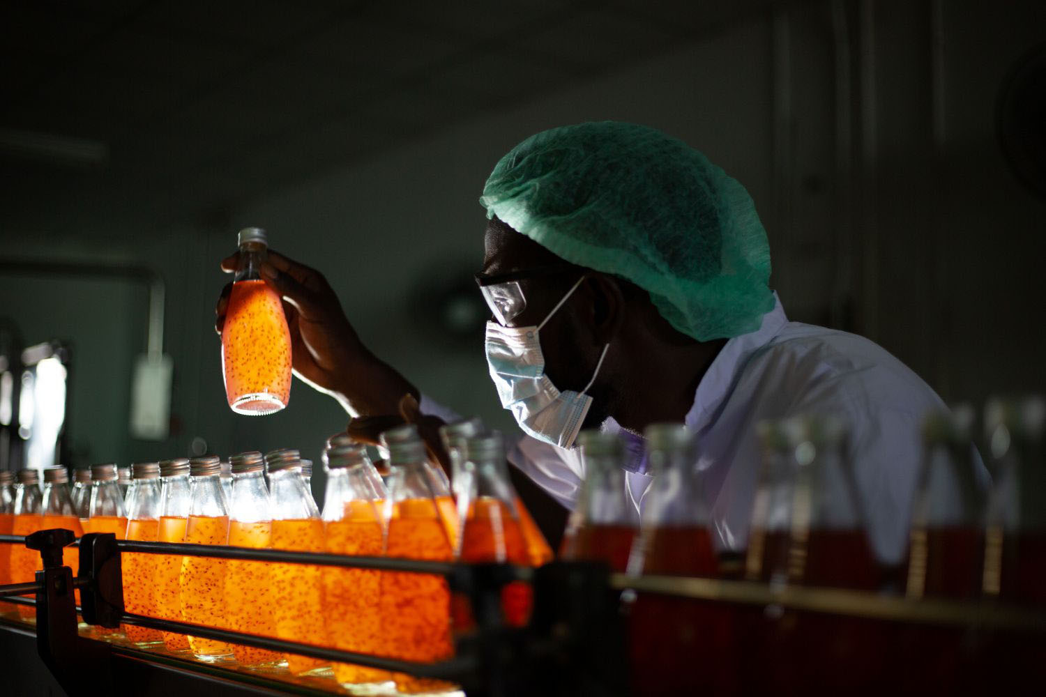 Worker inspecting drink product on bottling factory machinery