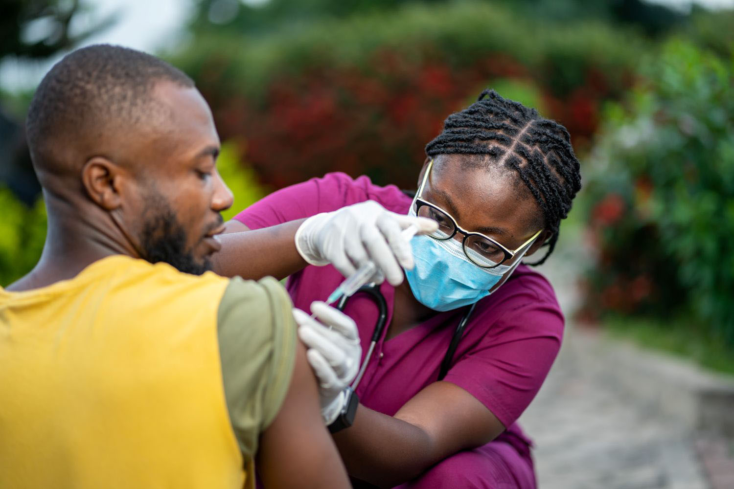  Young nurse wearing a face mask injecting an individual with a vaccine dose