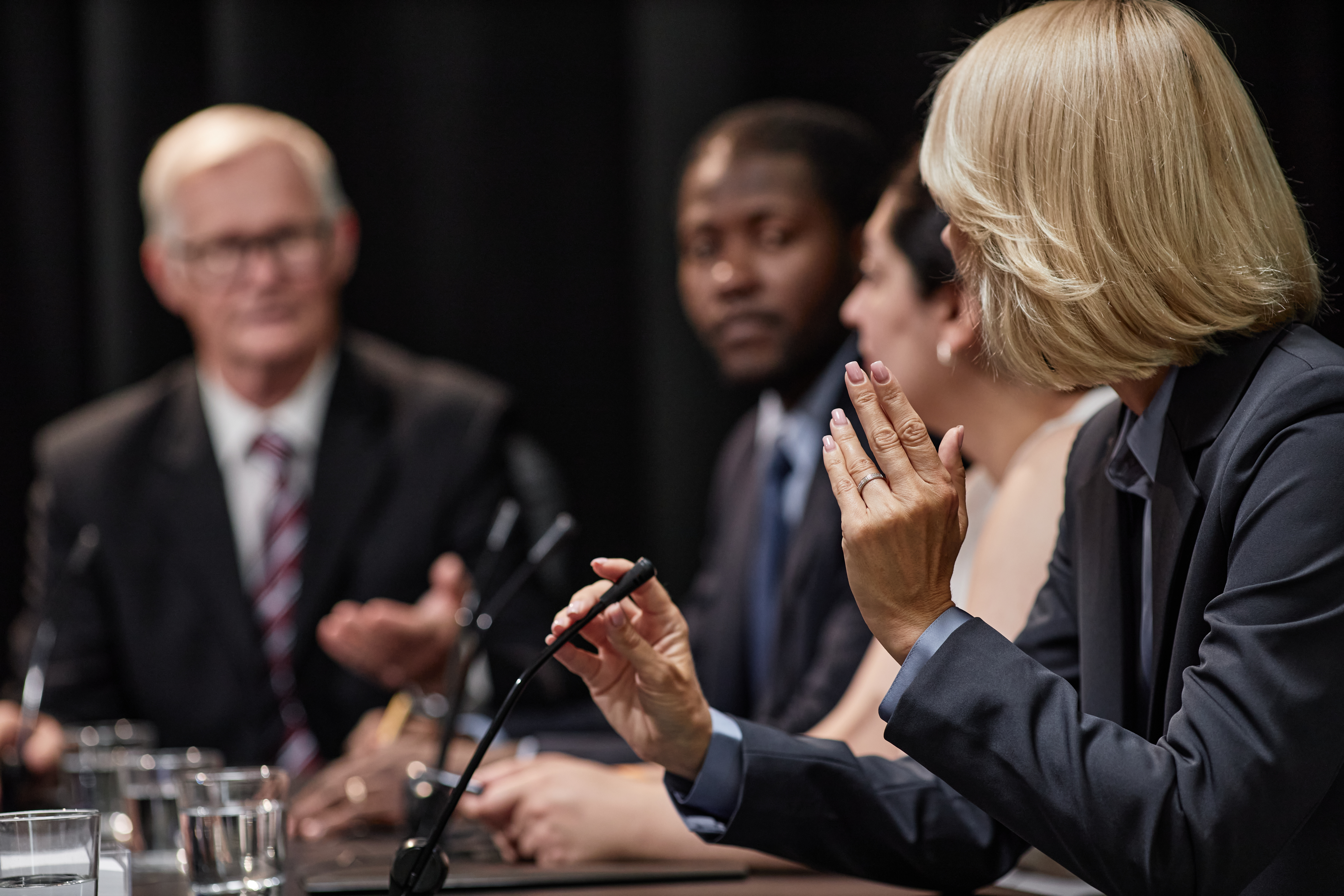Rear view of female official speaking into microphone asking politician question during political debate or press conference meeting room
