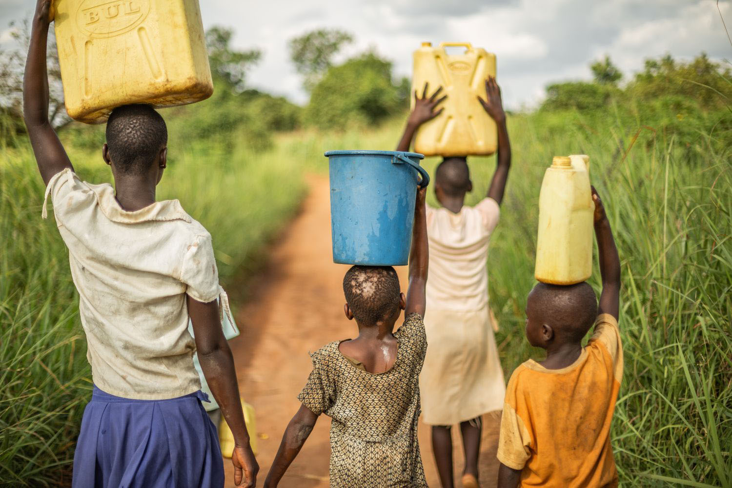 Group of young African children walking with buckets and jerrycans on their head