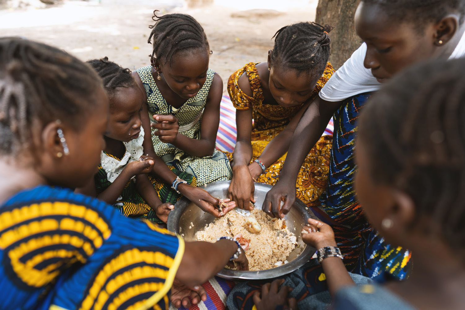 Group of young African girls sitting around eachother eating a big plate of rice and vegetables