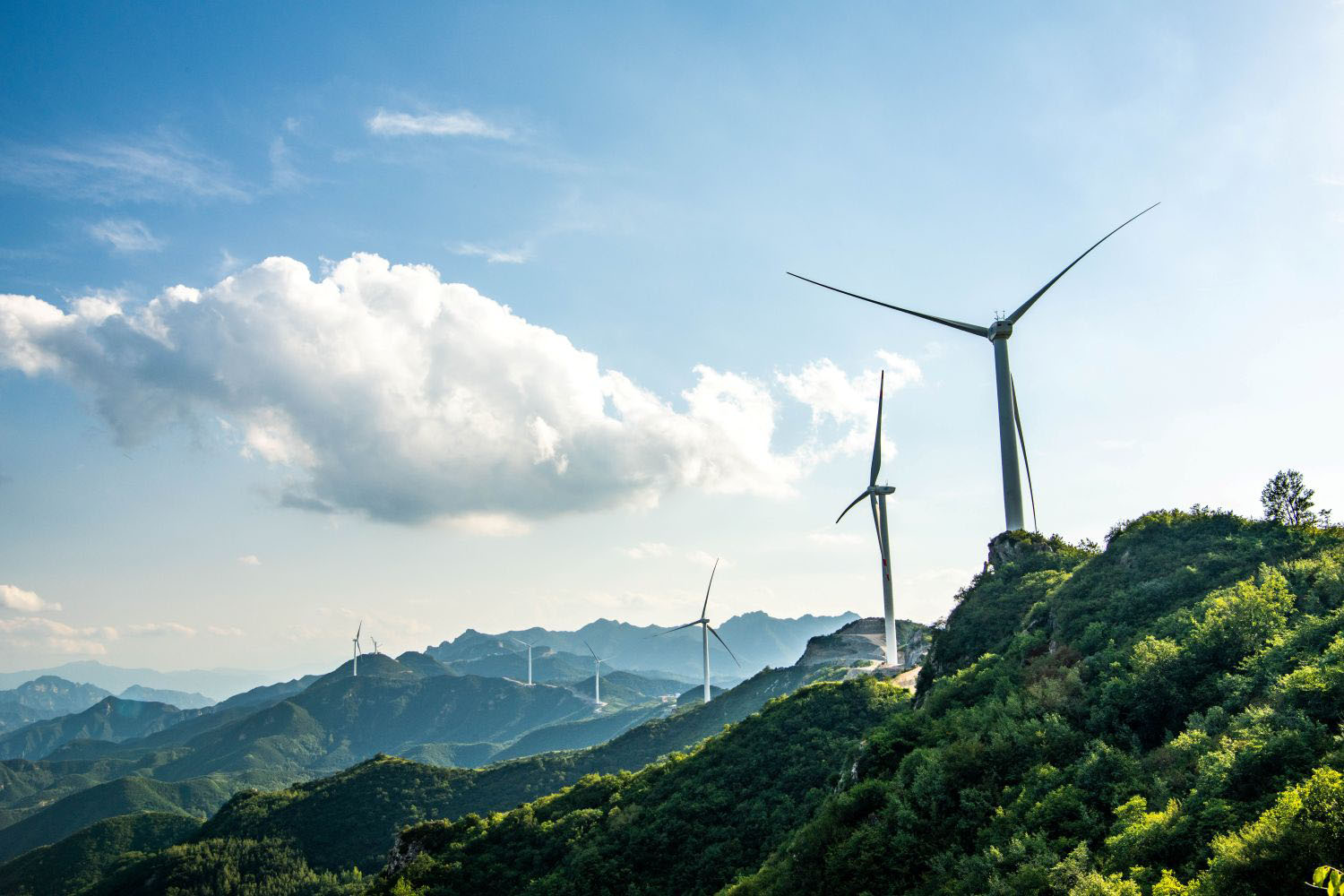 Wind turbines on green mountain ridges, representing renewable energy development and sustainable power generation.