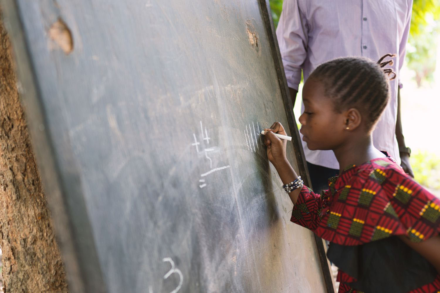 Child writing on a board in an outdoor classroom