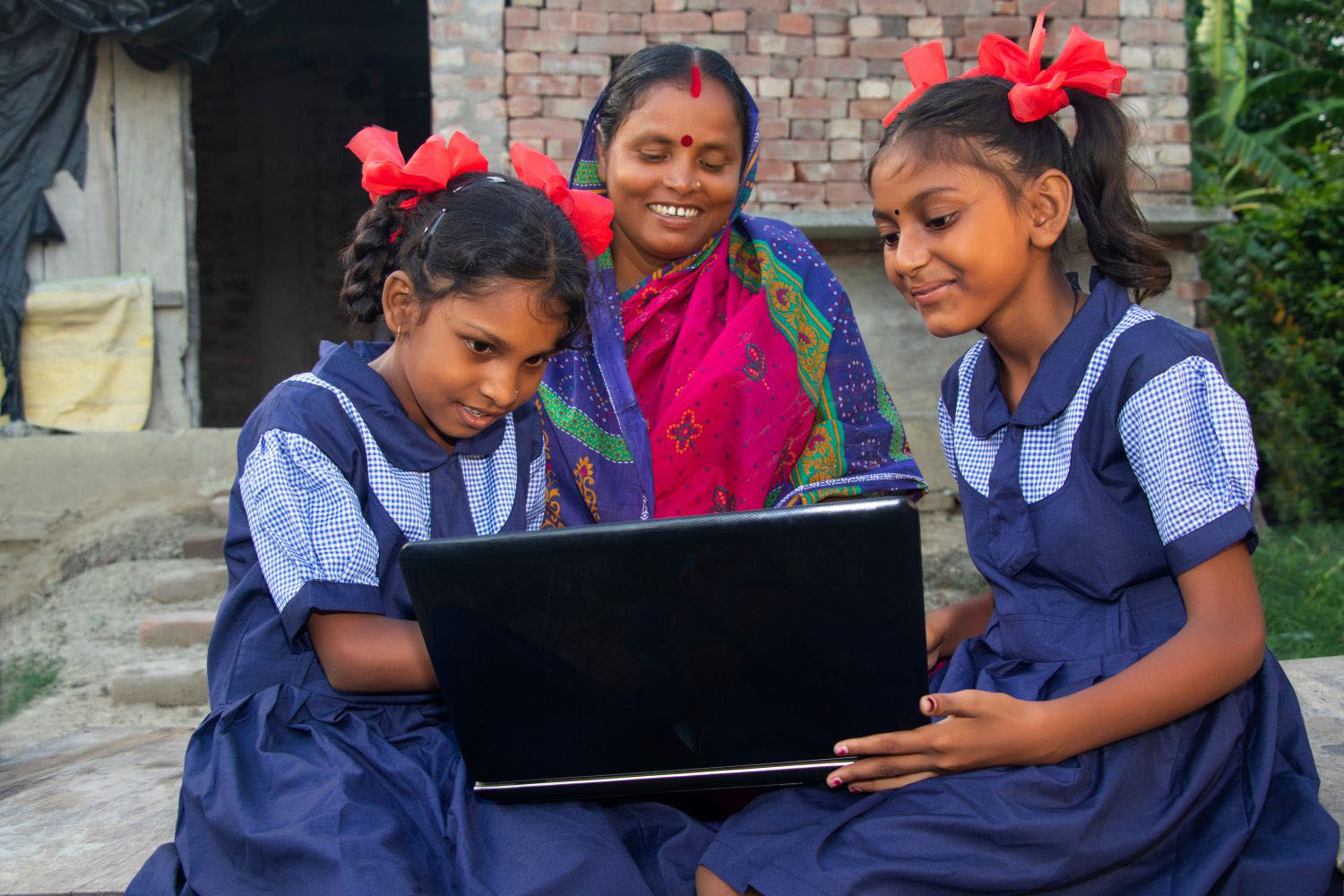 Students operating a laptop computer system while teacher sits beside them